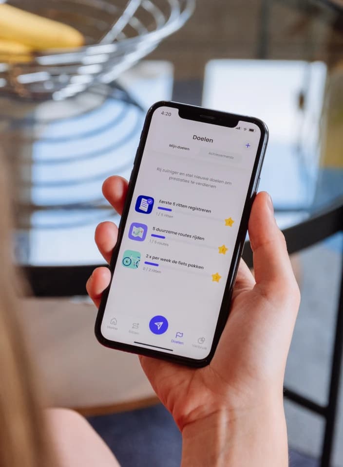 A hand holding a phone with a mobility app's goals screen, such as taking the bike twice a week